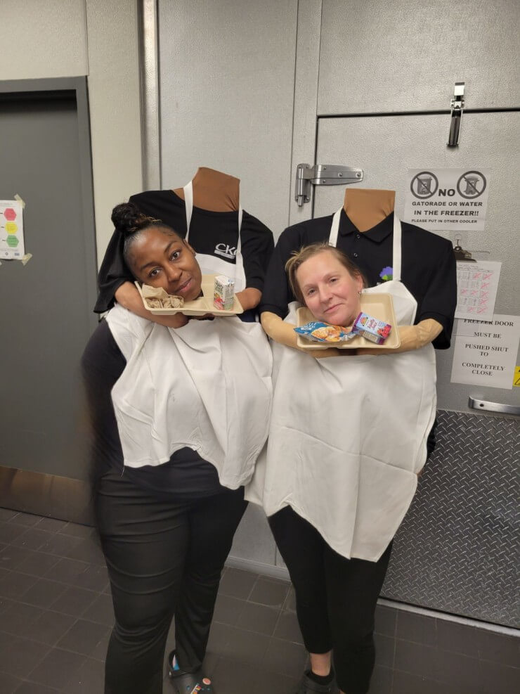 Two people in Halloween costumes who appear to be serving heads on a lunch tray